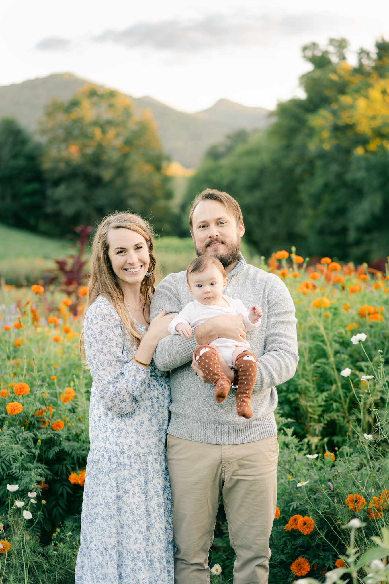 Mom, dad and baby smiling at the camera in Asheville NC flower field. Photo by Lauren Sosler Photography.