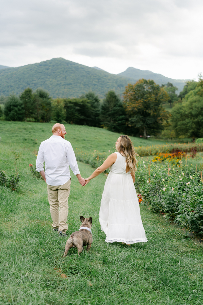 Couple walking with dog during their maternity session surrounded by flowers and mountains. Photo by Lauren Sosler Photography.