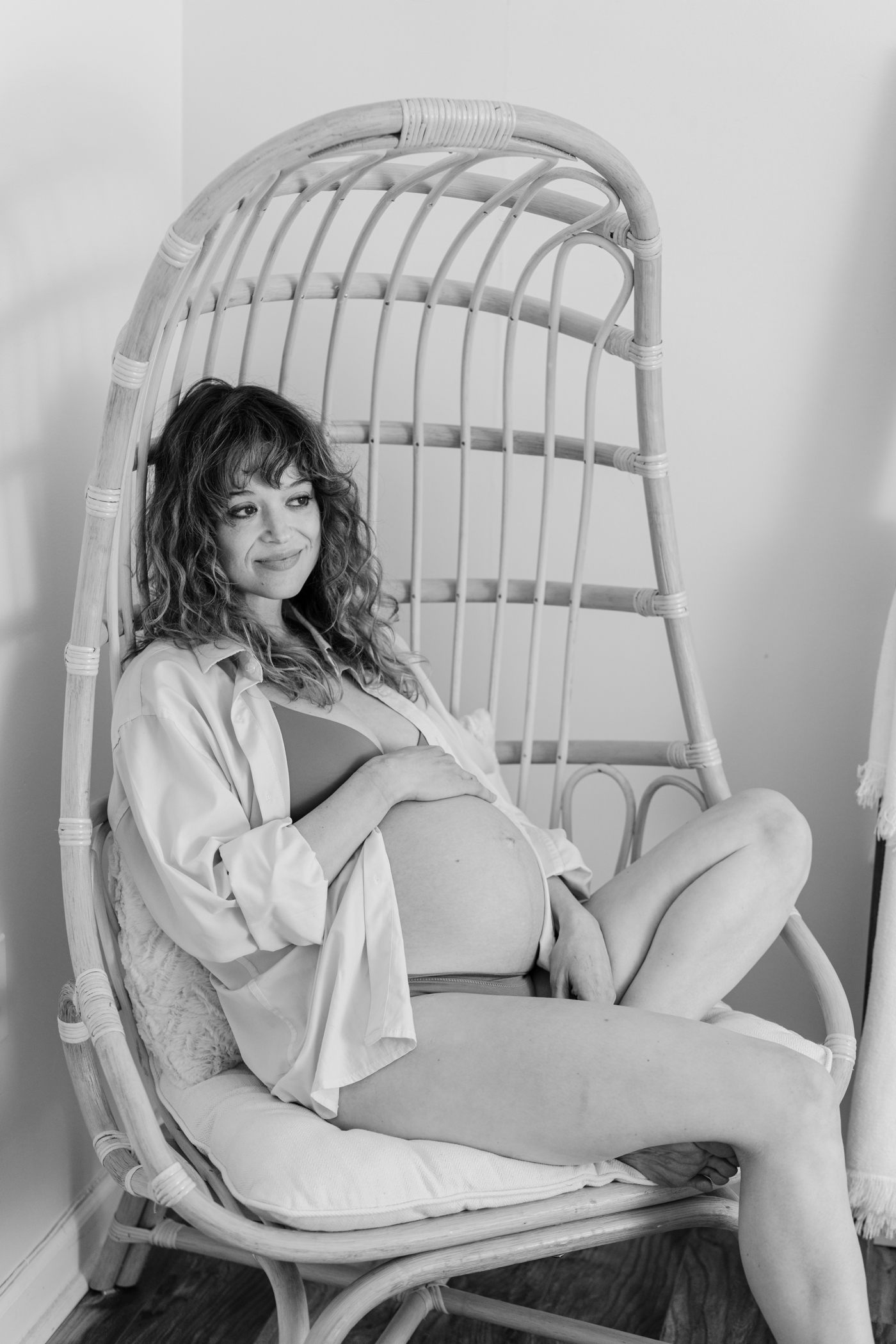Black and white image of Mom relaxed in wicker chair during studio maternity session with Lauren Sosler Photography