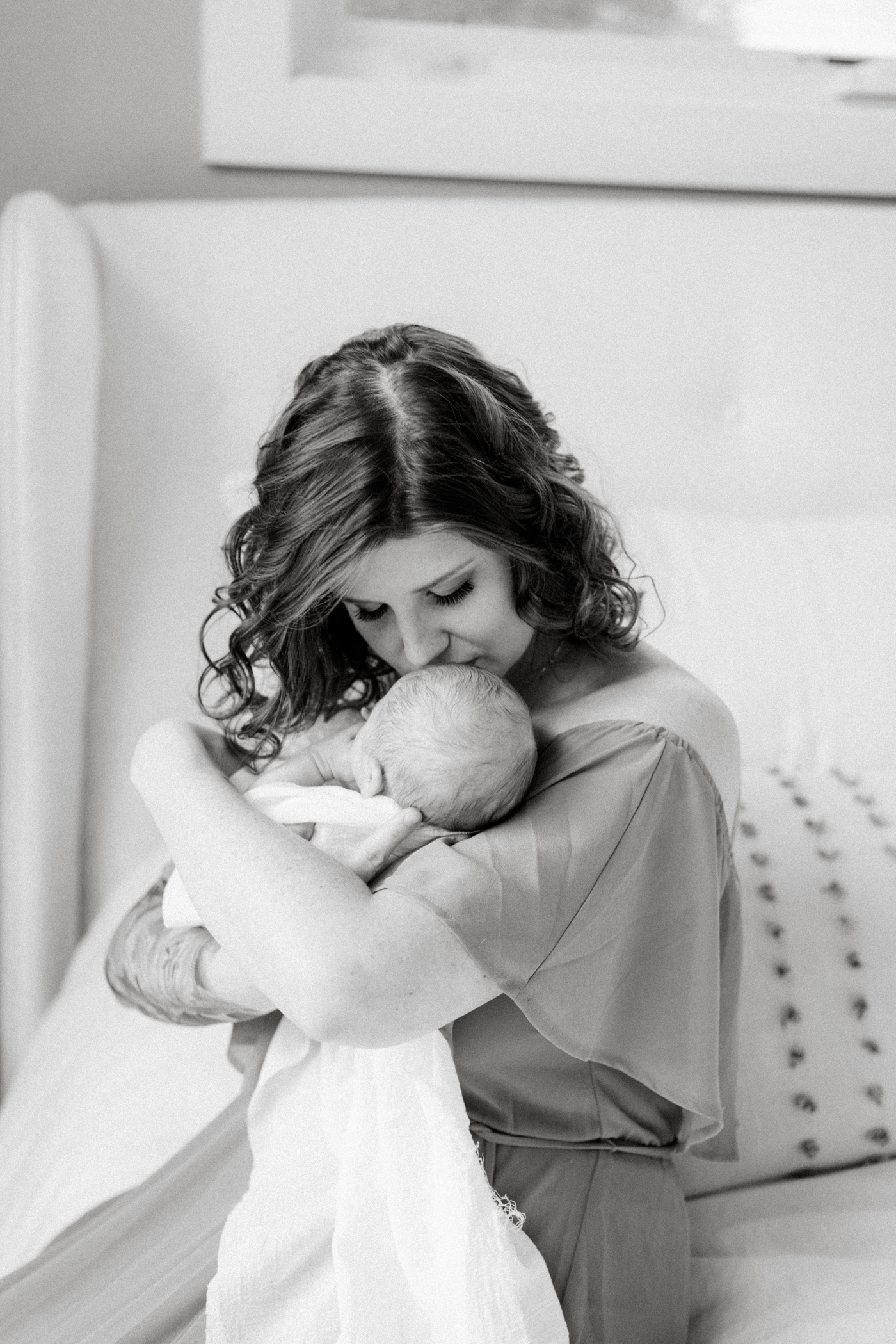 Black and white image of Mom kissing baby while sitting on bed. Photo by Lauren Sosler Photography.