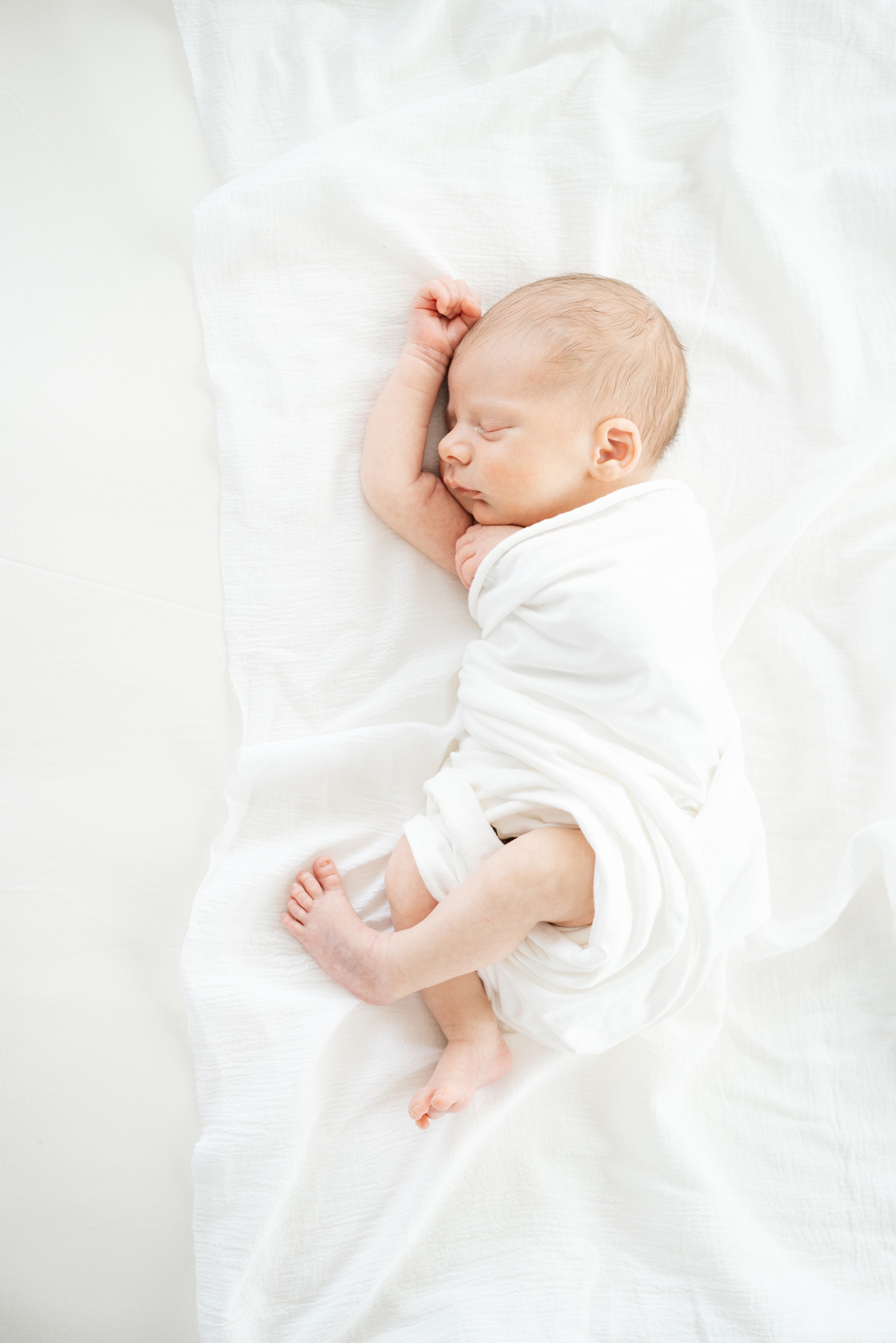 Baby boy sleeping in white swaddle during in-home lifestyle newborn session in Asheville NC. Photo by Lauren Sosler Photography.