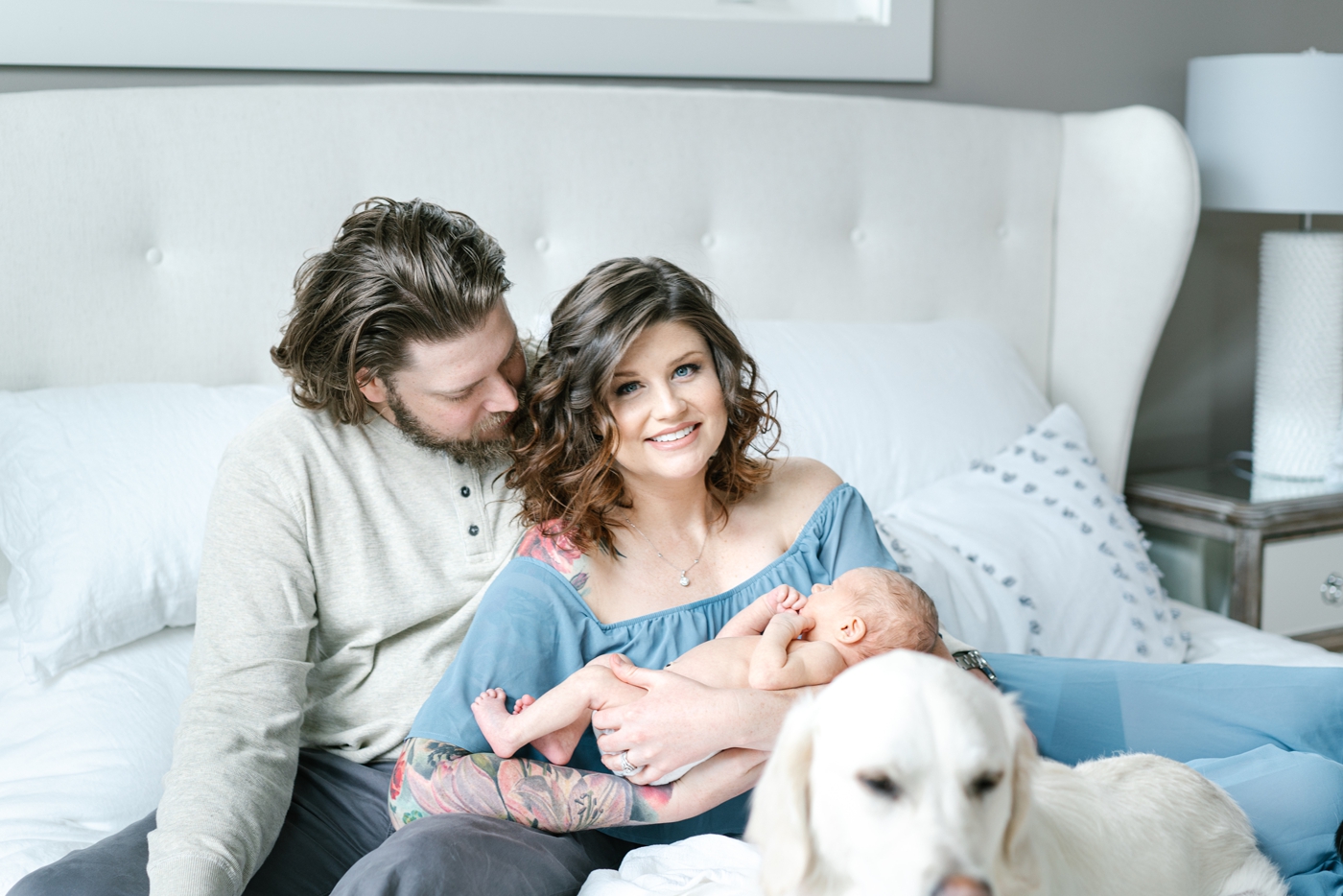 Mom and Dad holding baby while cuddled on the bed with dog. Photo by Lauren Sosler Photography.