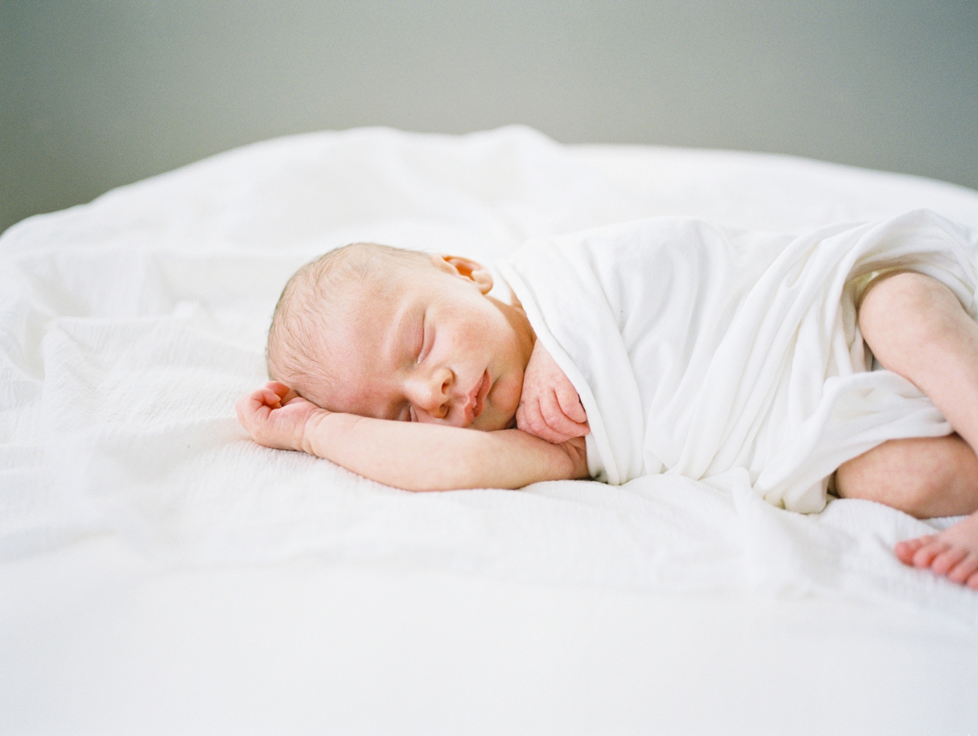 Film image of baby sleeping in white swaddle during in-home lifestyle newborn session in Asheville, NC. Photo by Lauren Sosler Photography.