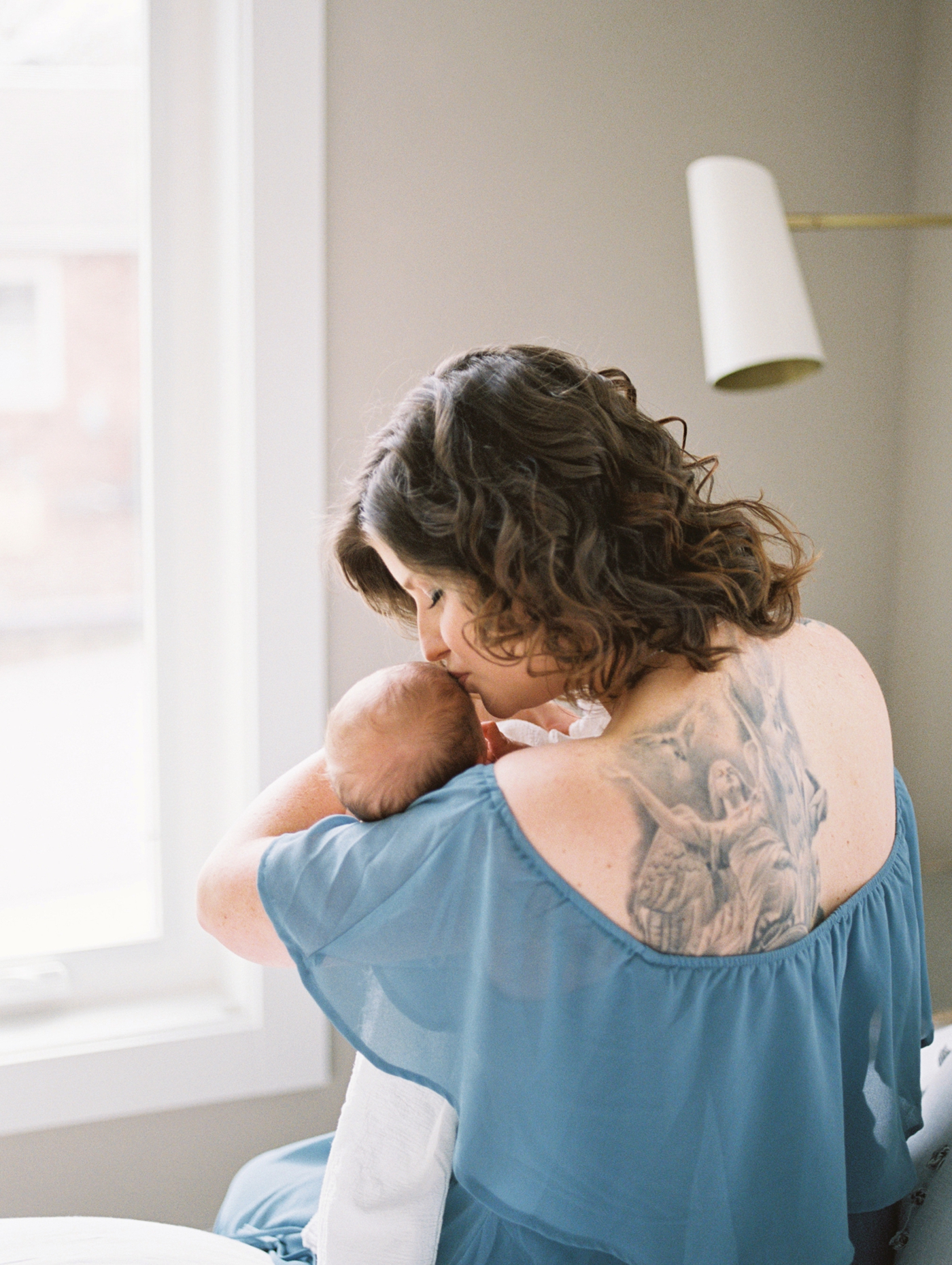 Film image of Mom kissing baby while sitting on the bed. Photo by Asheville newborn photographer, Lauren Sosler Photography.