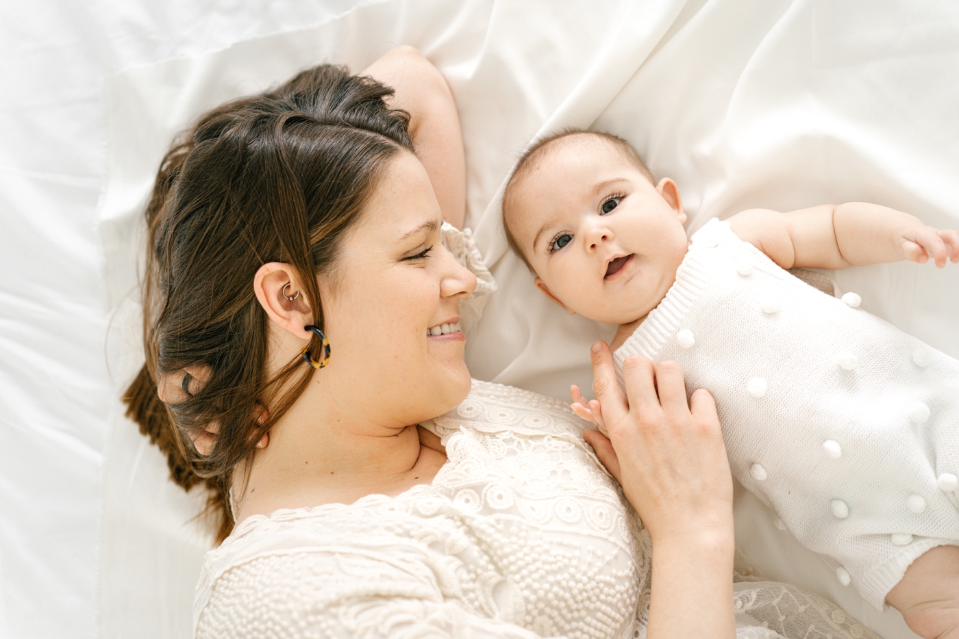 Mom laying on bed with baby girl during studio milestone session. Photo by Lauren Sosler Photography.