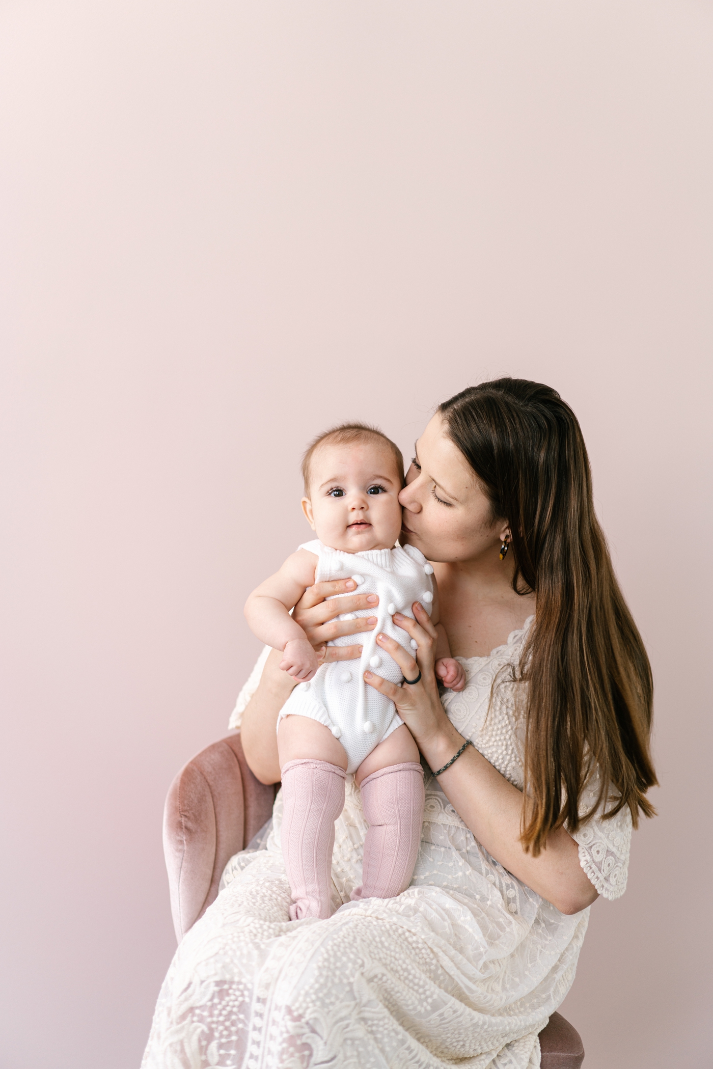 Mom kissing baby's cheek in front of pink backdrop. Photo by Lauren Sosler Photography.